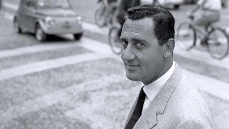 una foto in bianco e nero di alberto sordi per l strade di roma