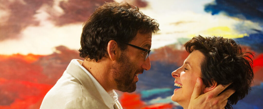 clive owen e juliette binoche si abbracciano dvanti a un quadro in una scena del film